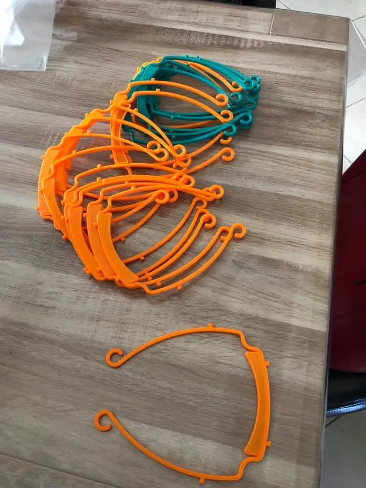 Montures de visières imprimées en 3D, orange et turquoise, posées sur une table